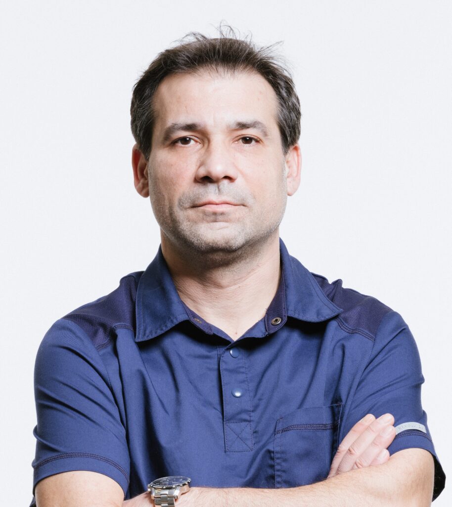 Лекар невролог с сериозен поглед, стоящ с кръстосани ръце.